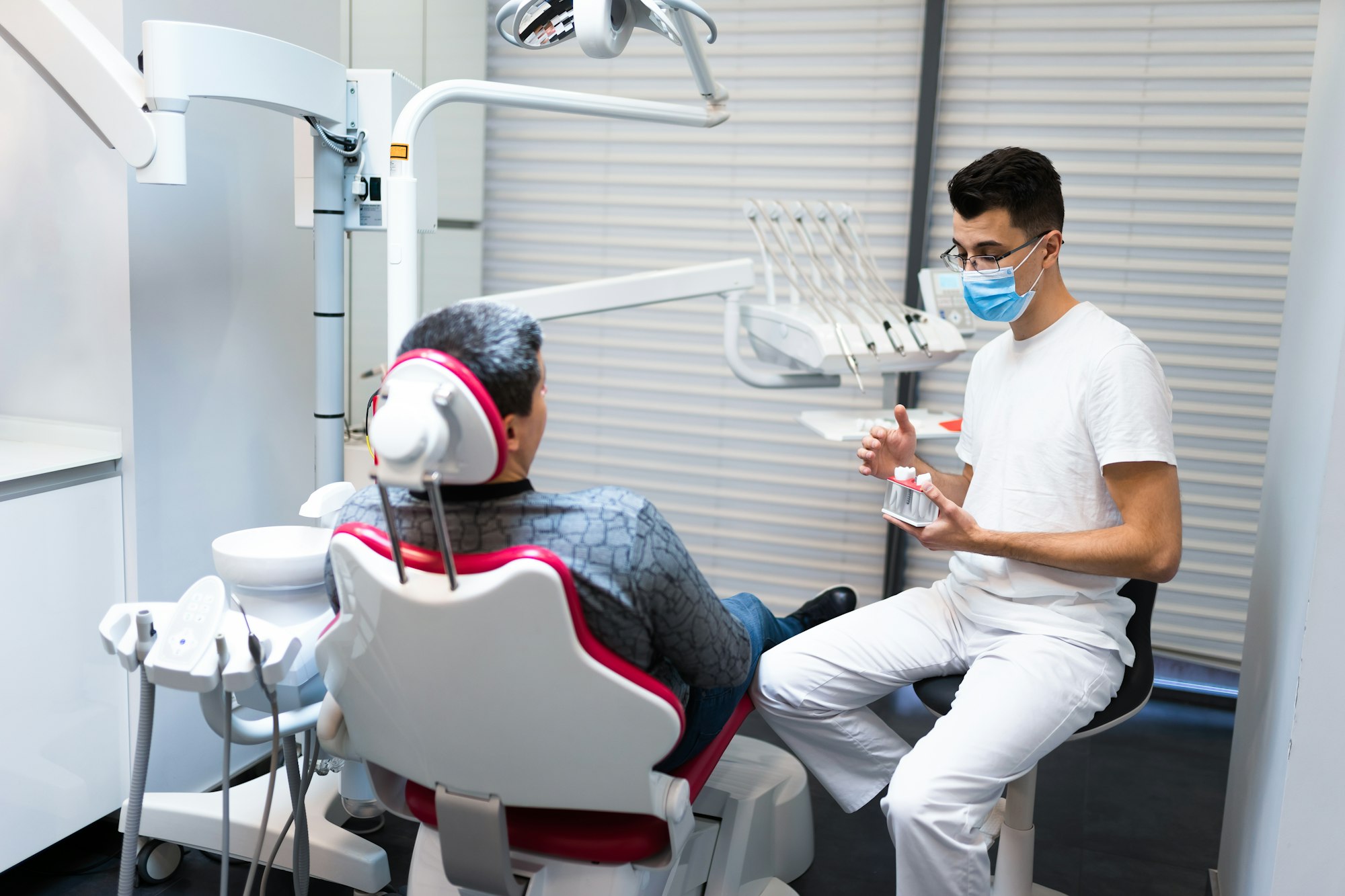 Dental surgeon with dental crown in hands model talks to patient about prosthetics.