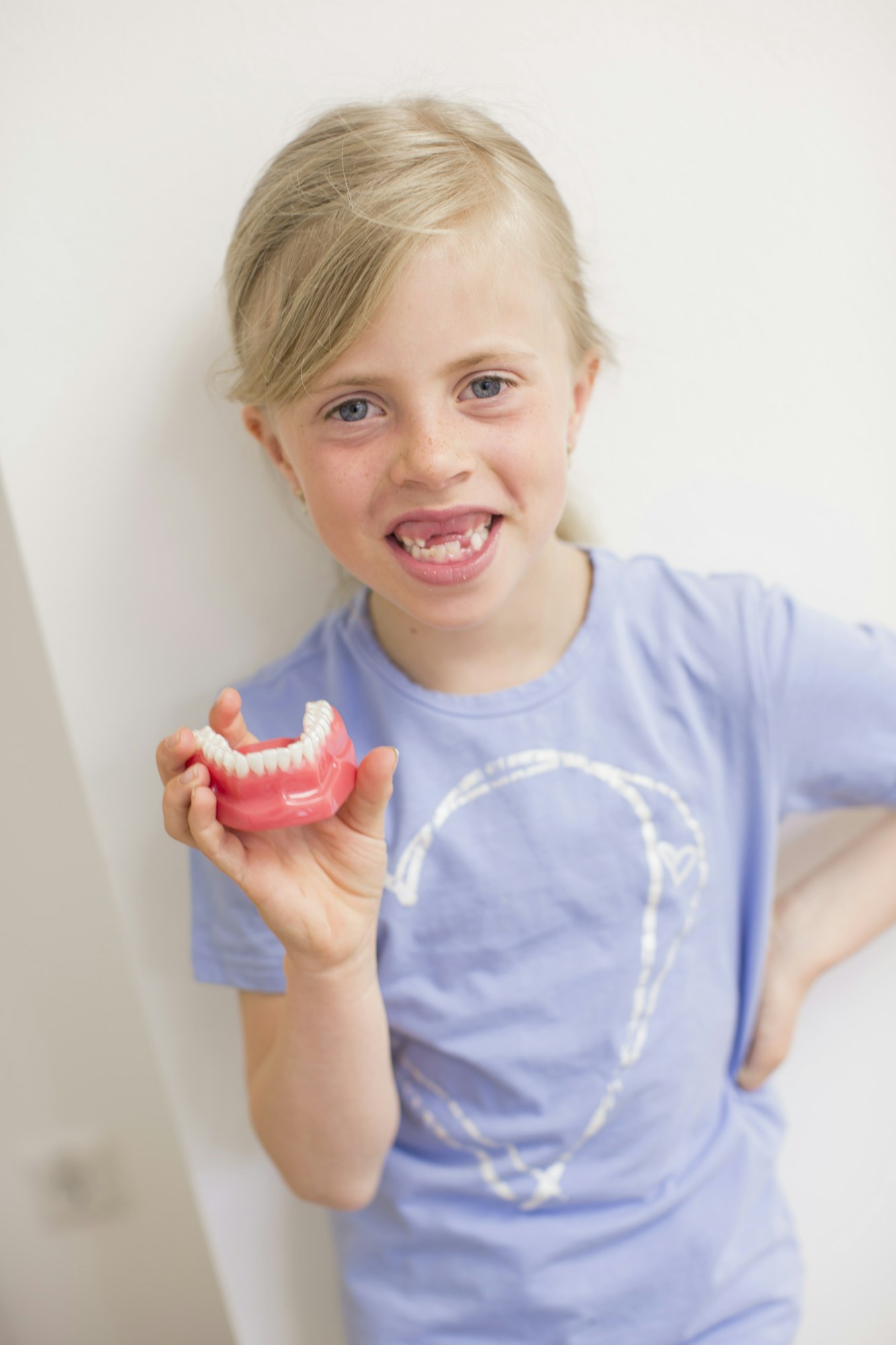 Girl with missing teeth holding dentures looking at camera smiling