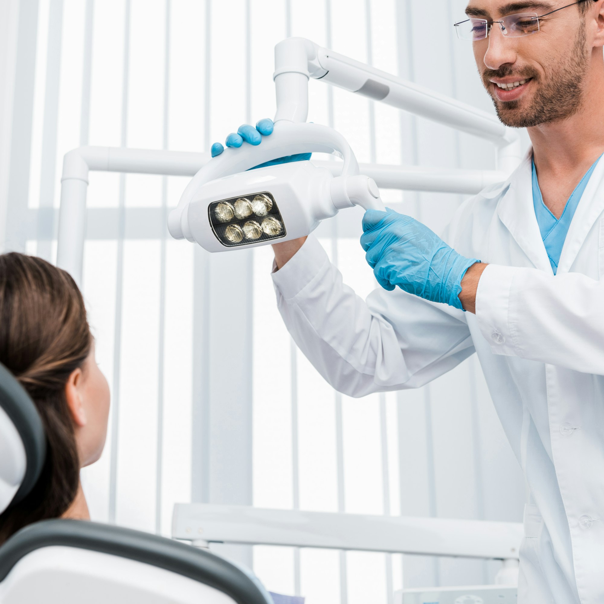 selective focus of handsome dentist in latex gloves touching medical lamp near patient