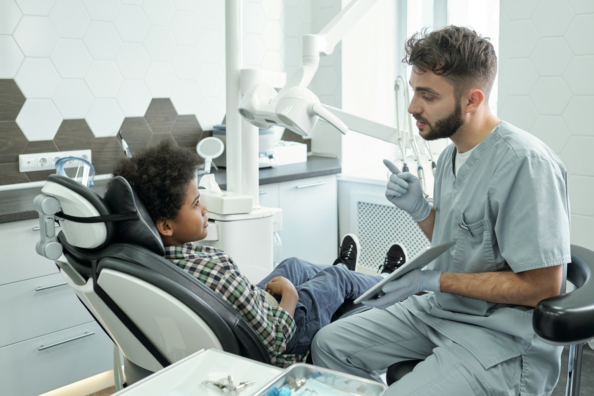 Young confident dentist with tablet consulting little patient