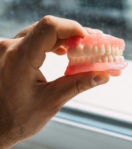 An elderly man holds a denture. A man is holding dentures in his hands. Removable dentures flexible