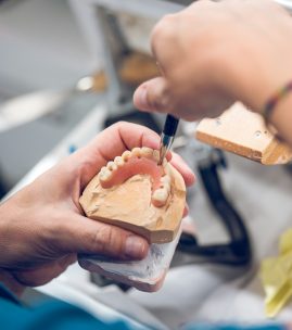 Crop dental technician carving denture while working in lab