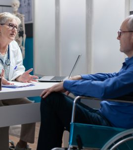 Physician talking to man with disability at annual checkup visit in medical cabinet