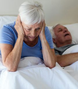 Senior woman getting disturbed with man snoring on bed